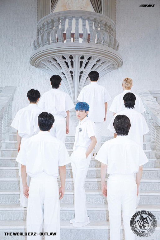 Eight men in white with one man with blue hair looking at camera under a white balcony