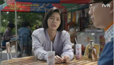 A girl leaning against a table with cans of soda talking to a boy slightly out of frame