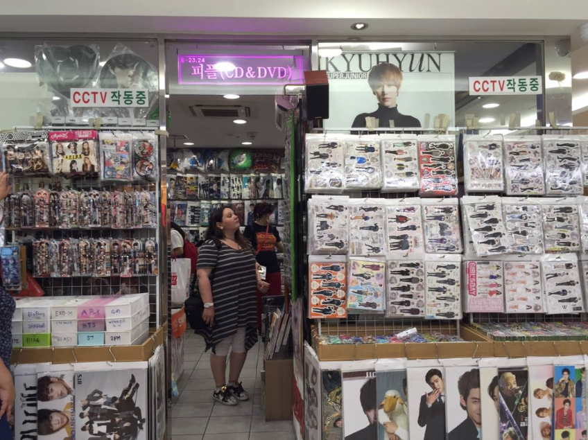 A woman looking up between a stack of K-pop albums and posters featuring Kyuhyun