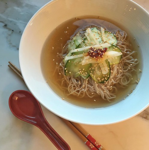 A bowl of naengmyeon beside a wooden spoon and chopsticks