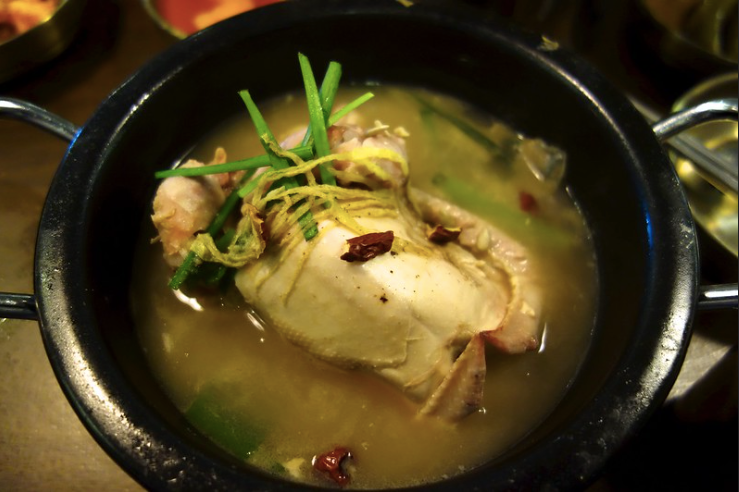 A black pot with a whole chicken and samgyetang broth inside