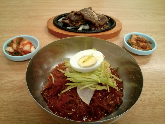 A bowl of bibim-guksu with three banchan dishes behind it