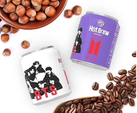 A white canned coffee and purple canned coffee with a bowl of hazelnuts and a bowl of coffee beans