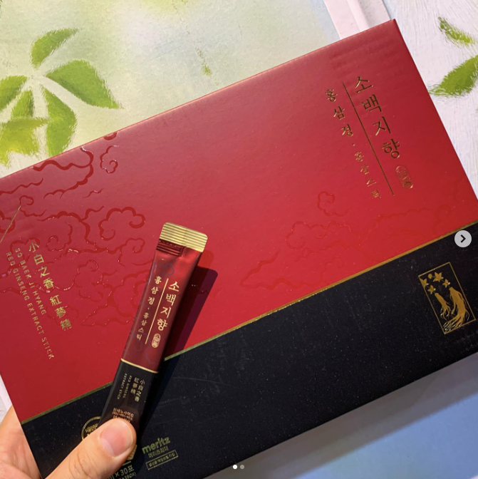 A box of red ginseng extract with a stick and hand on top