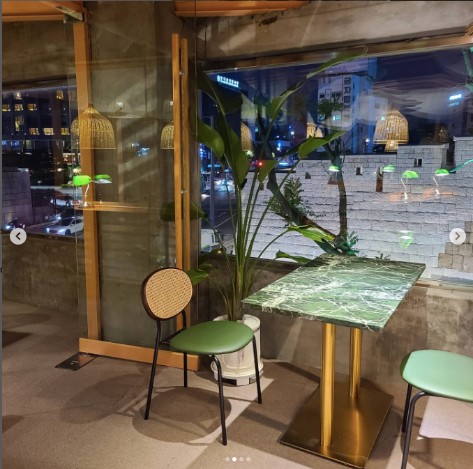 A couple of green-seated chairs and a green table by a window with ferns nearby