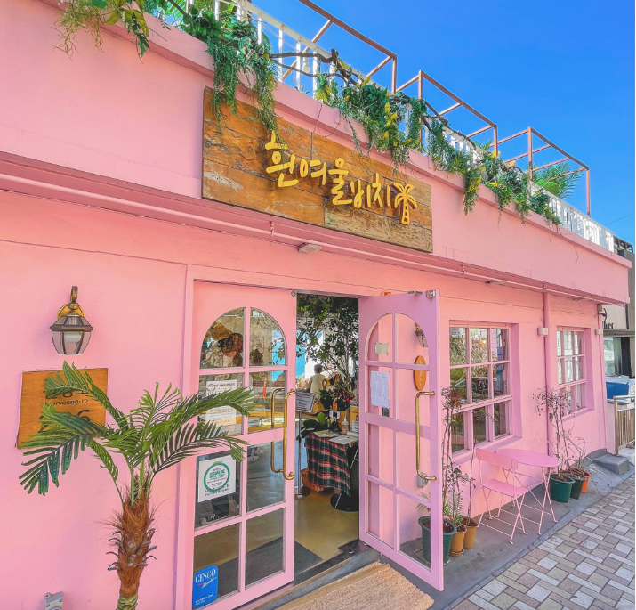 A pink building with palm trees and an open screen door