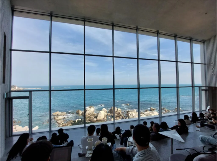 People sitting in front of wall of windows overlooking ocean and beach