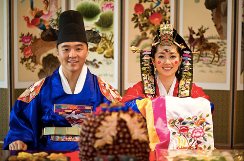 Groom in blue hanbok and bride in red in front of date display