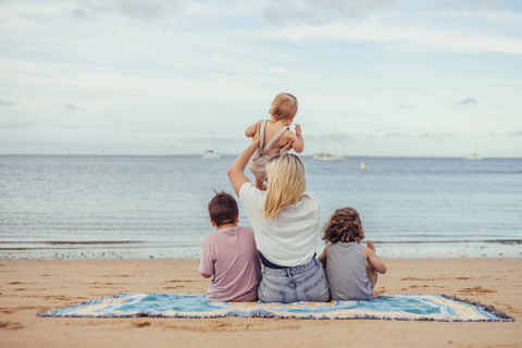 Mum and 3 sons sitting on a beach blanket on the sand