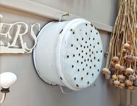 white enamelled metal colander hanging on a grey wooden shed wall