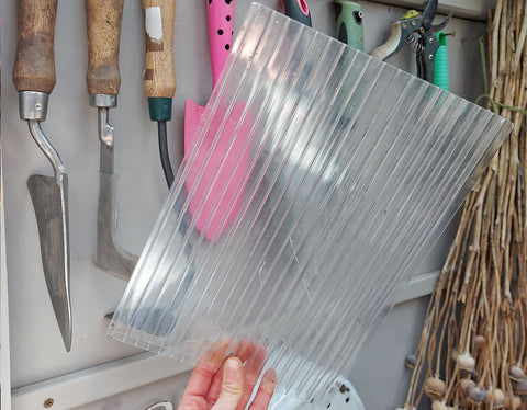 hand holding a small sheet of plastic polycarbonate sheeting in grey shed