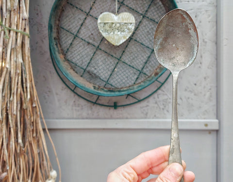 Hand holding an old dessert spoon with a spoil sifter behind