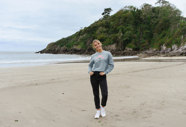 woman on a beach with blue jumper with a pale pink rose flower on it