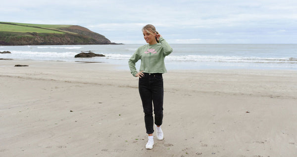 woman on a beach with green jumper with a pale pink dainty bess rose on it