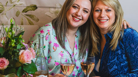 A woman and her mother smiling, drinking rosé next to flowers