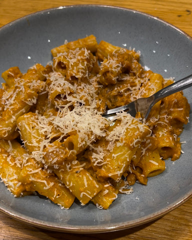 A blue pasta bowl with pumpkin rigatoni sprinkled with parmesan cheese. A fork is lifting up a piece of pasta