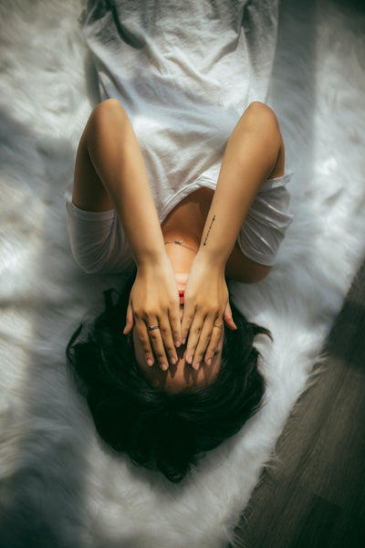 woman lying with back down on bed with her hands on her face