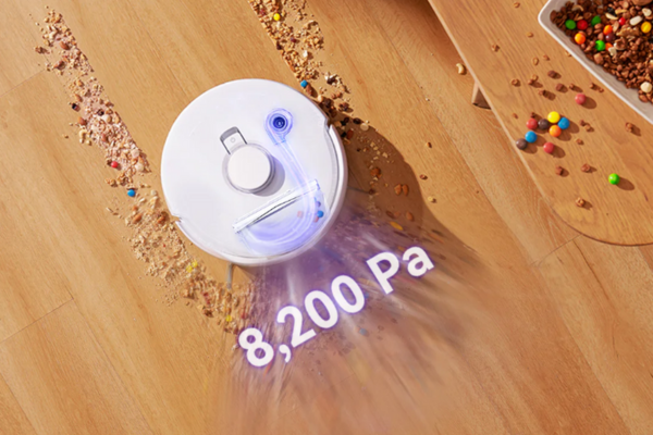 Robot vacuum cleaner showing suction power of 8,200 Pa on a wooden floor with scattered debris.