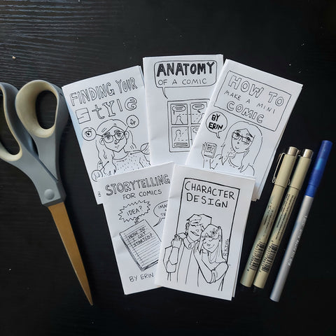 5 mini comics laid on a black table, with a set of scissors and markers