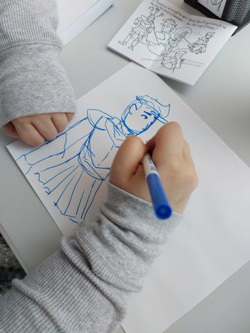Close up of a person drawing a cartoon character in blue marker on a sheet of paper