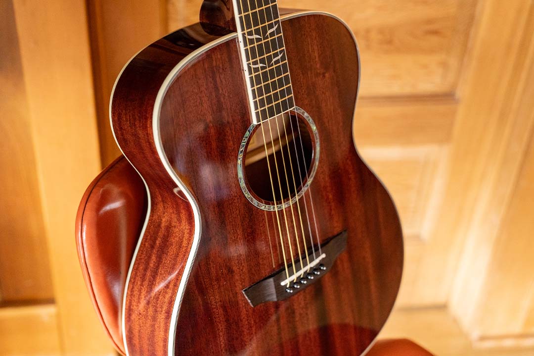 Mahogany solid top guitar with natural gloss finish and abalone rosette sitting on a chair