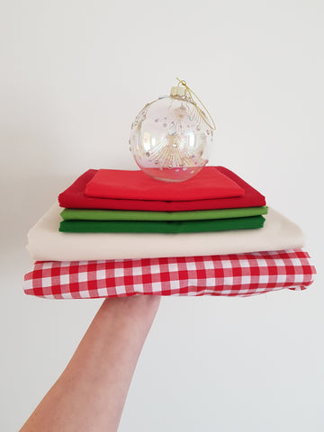 Hand holding up a pile of fabric in shades of cream, red and green with a christmas bauble sitting on top