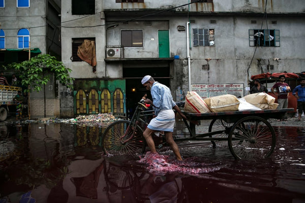 A man walks through colored rainwater past a dyeing factory in Shyampur in June 2018. Its waste is dumped into the Buriganga river in Dhaka, Bangladesh. Credit: Allison Joyce/Getty Images