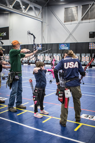 Three archers stand on the shooting line at the Lancaster Archery Classic. A youth archer in the girl's compound class aims her bow.