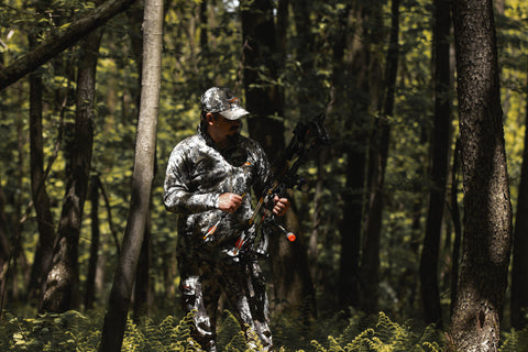 Josh Grine wearing SITKA Gear Elevation II Camo is concealed by his clothes along with the colors of the woods and shade of the trees.