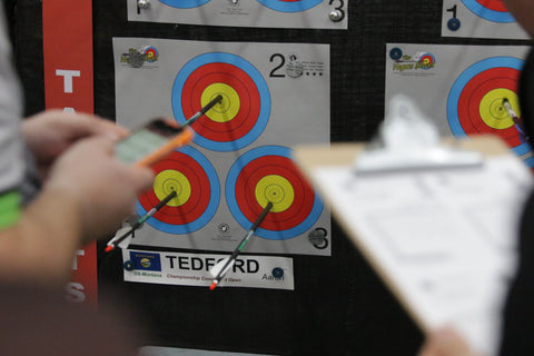 Two archers, one with a tablet and the other with a score card, score arrows at the Vegas Shoot in front of Aaron Tedford's target.