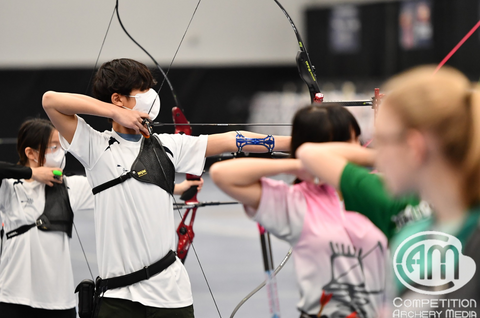 Two youth recurve archers stand on the shooting line at full draw.