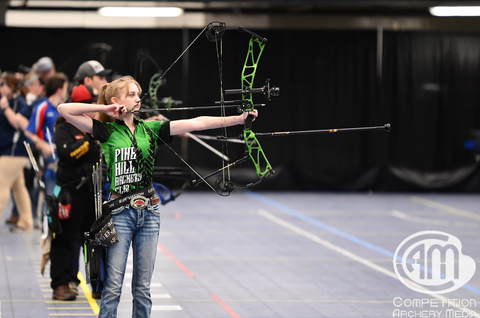 A young female archer aims her bow at the target, ready to hit the center 11.