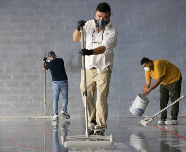 Contractors working a large industrial warehouse floor & installing an epoxy-based moisture barrier seal.