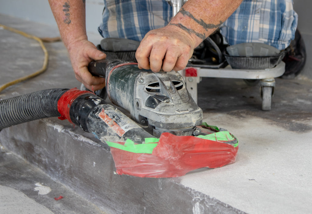 A contractor using an angle grinder tool to prepare a concrete surface for epoxy resin installation.