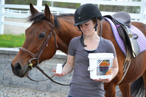 Woman and horse standing holding a bottle of pills and Bute-Less Performance Supplement