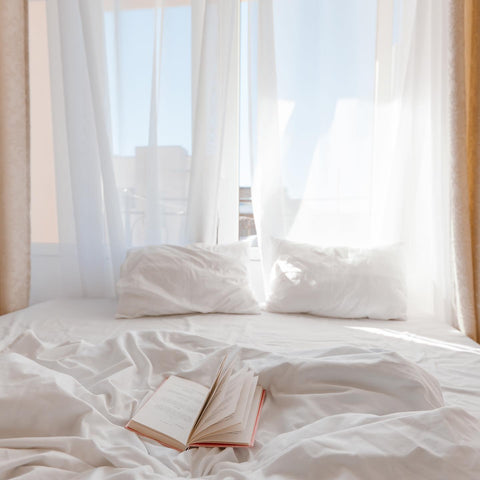 A white bed with custom pillows, natural light coming in the window, and a book on the sheets