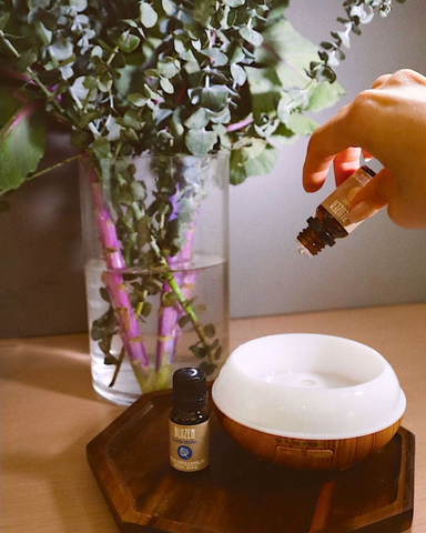 A person pours BluZen essential oil into an air diffuser