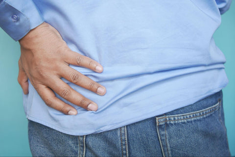 Person wearing jeans and a blue shirt with their hand on the lower back indicating lower back pain