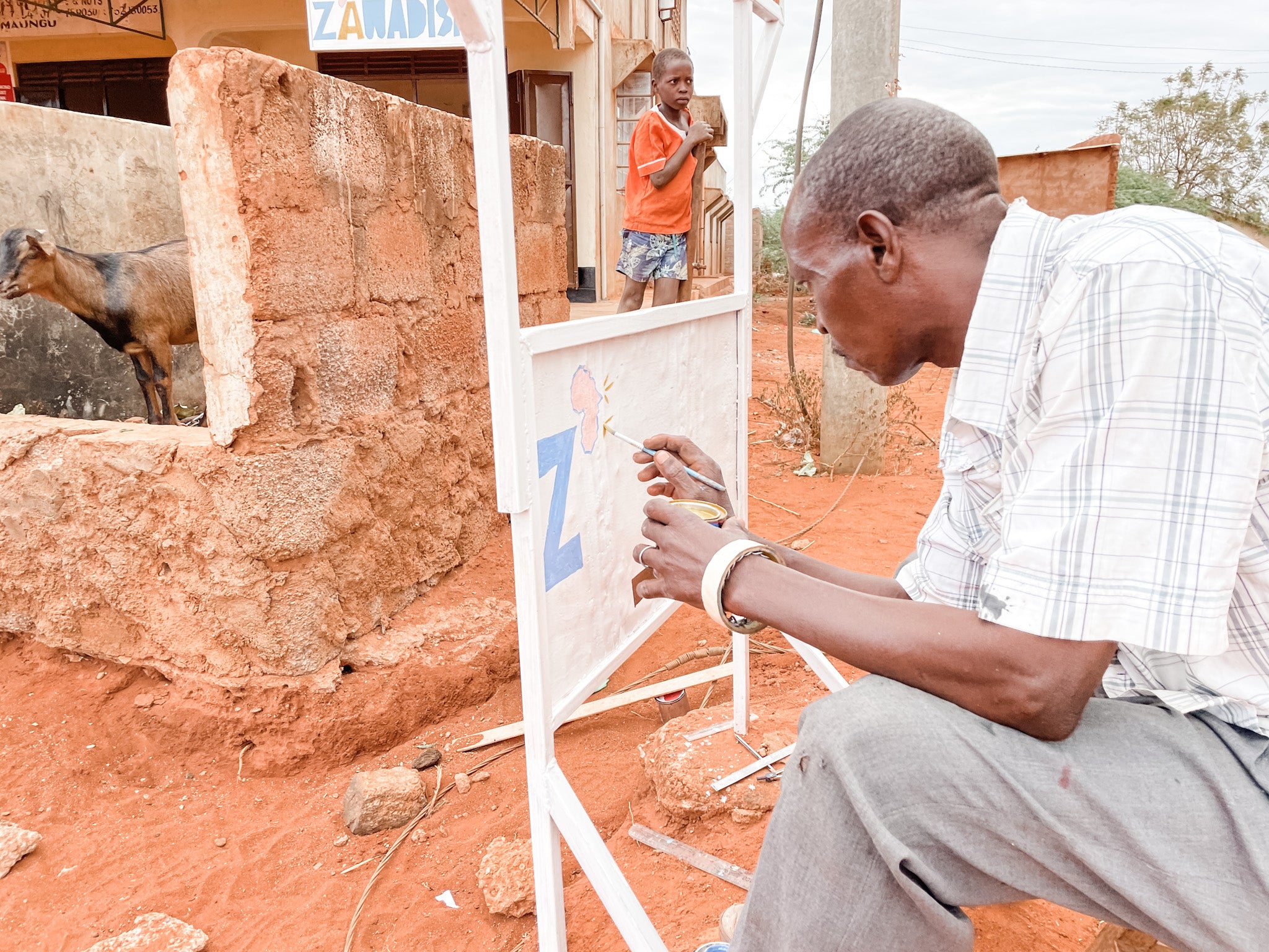 A man paints a sign outside of the Zawadisha shop in Kenya