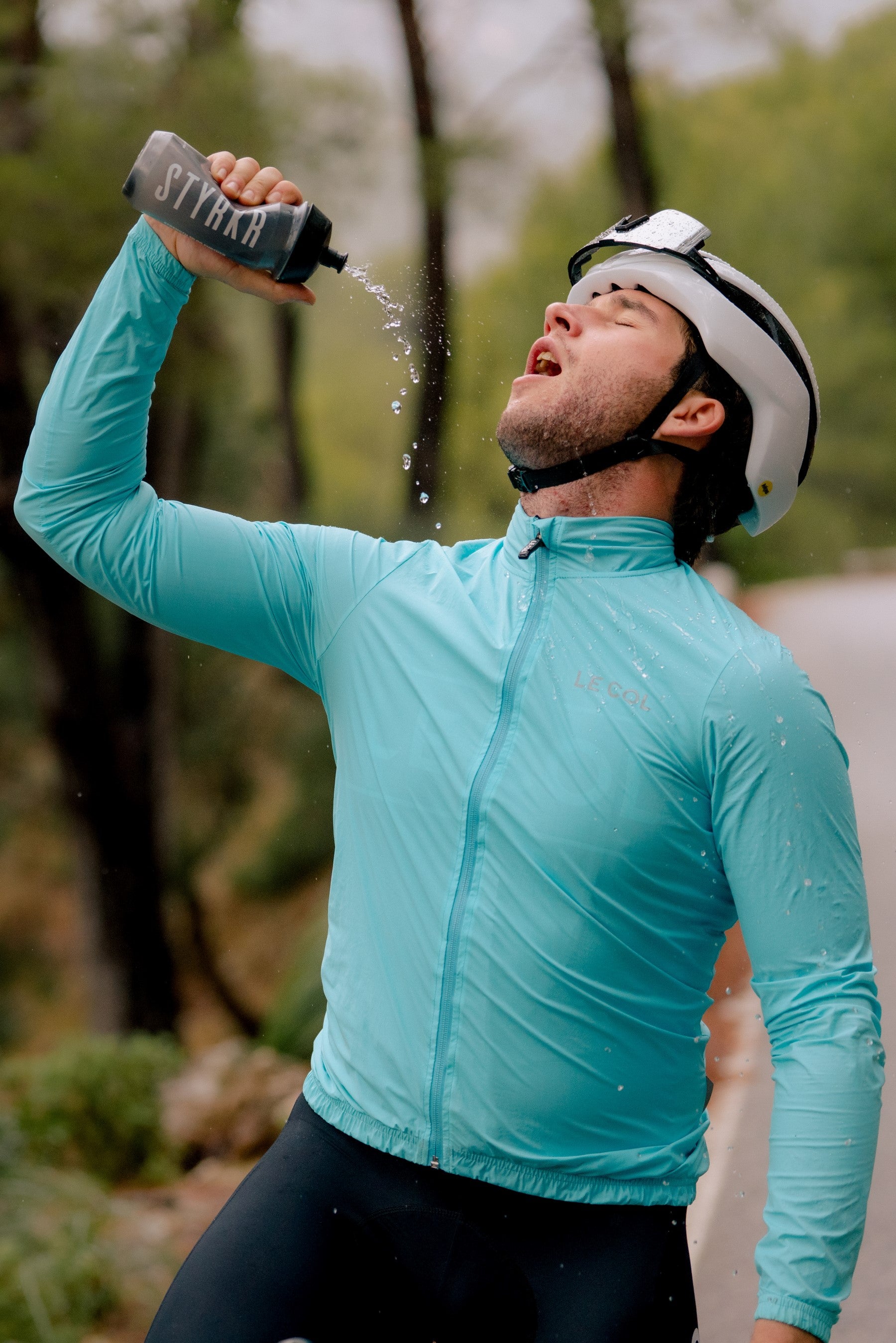 cyclist with helmet pouring water from a bottle on himself to cool down