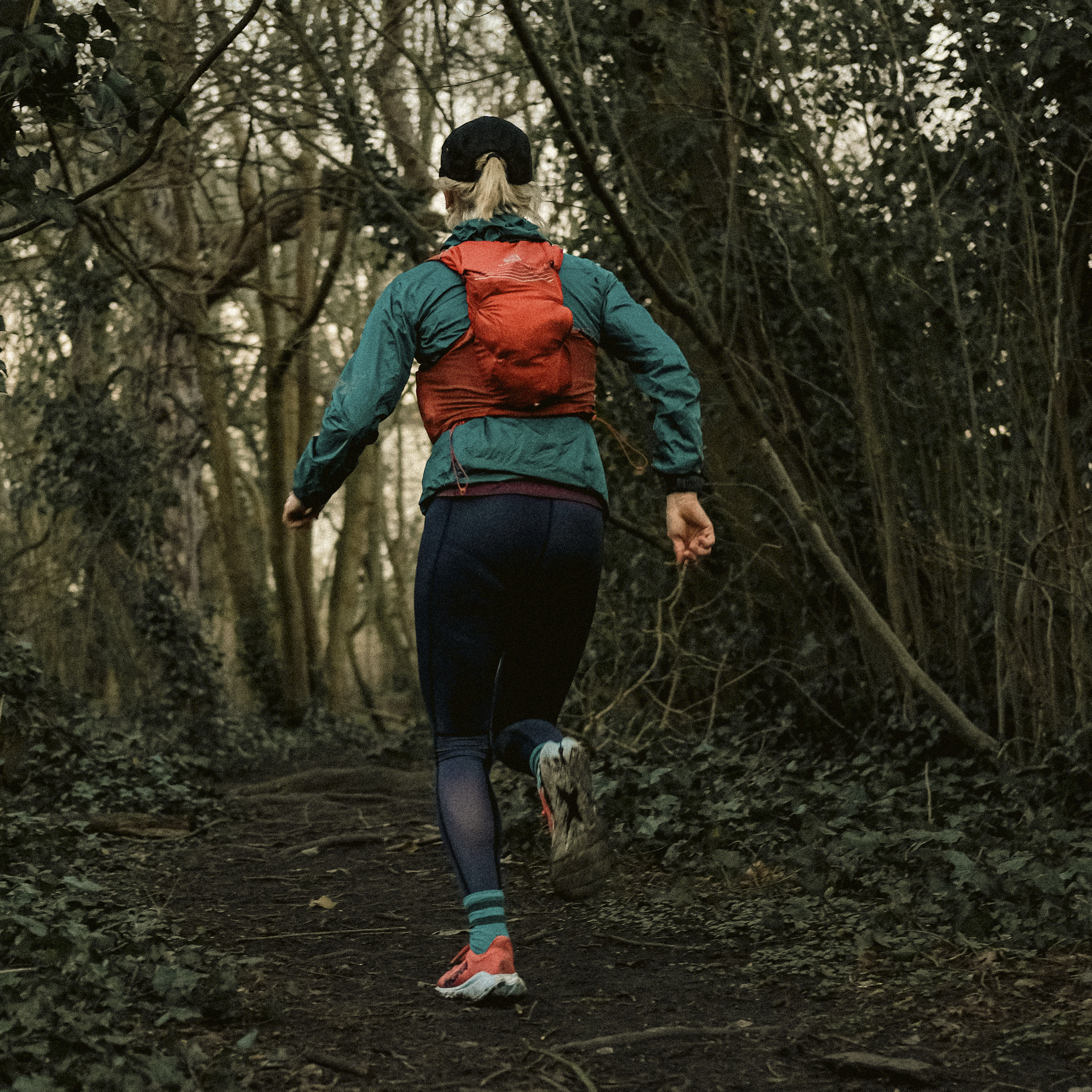 woman running away from camera into the woods with orange backpack 