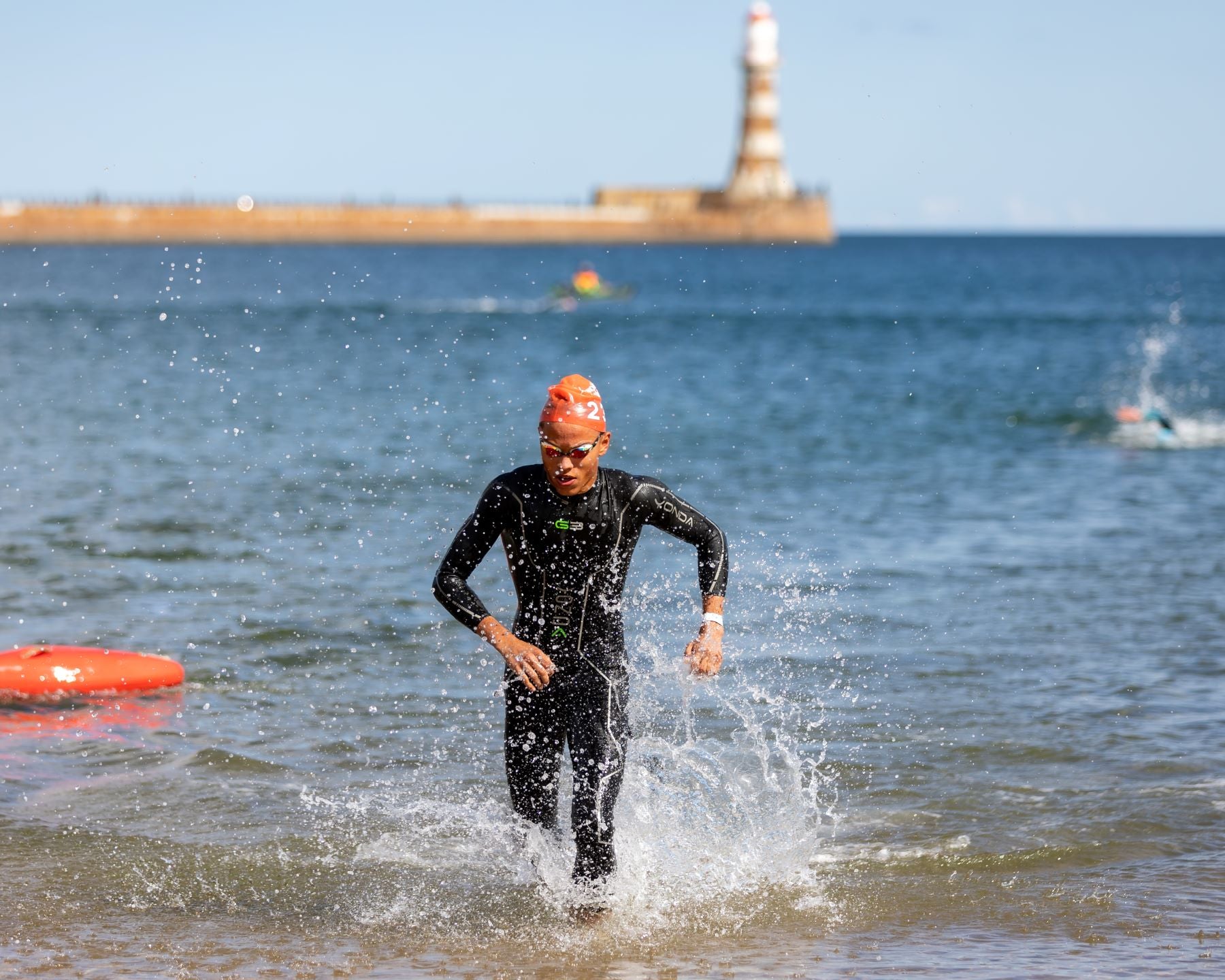 styrkr athlete solomon running out of the sea wearing wet suit and cap