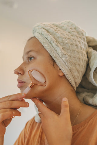 A young woman using rose quartz face roller on her cheek