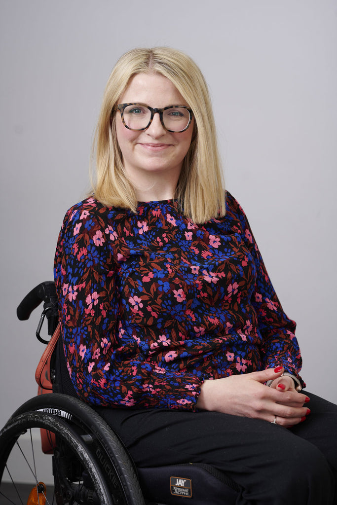 Jo Williams smiling in a floral top seated in her wheelchair