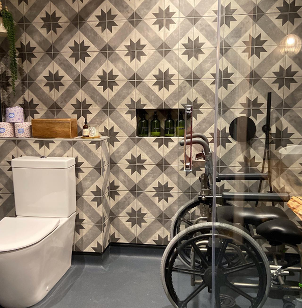 Wheelchair in a shower area of JO's bathroom with geometric black and white patterned tiles