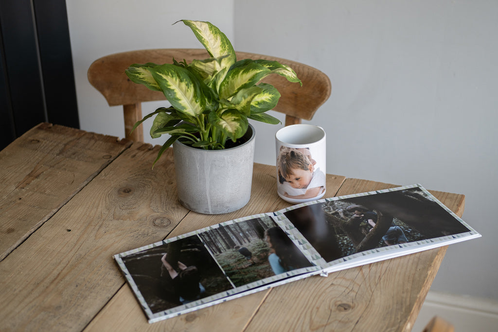 Open photo book on wooden table next to plant.