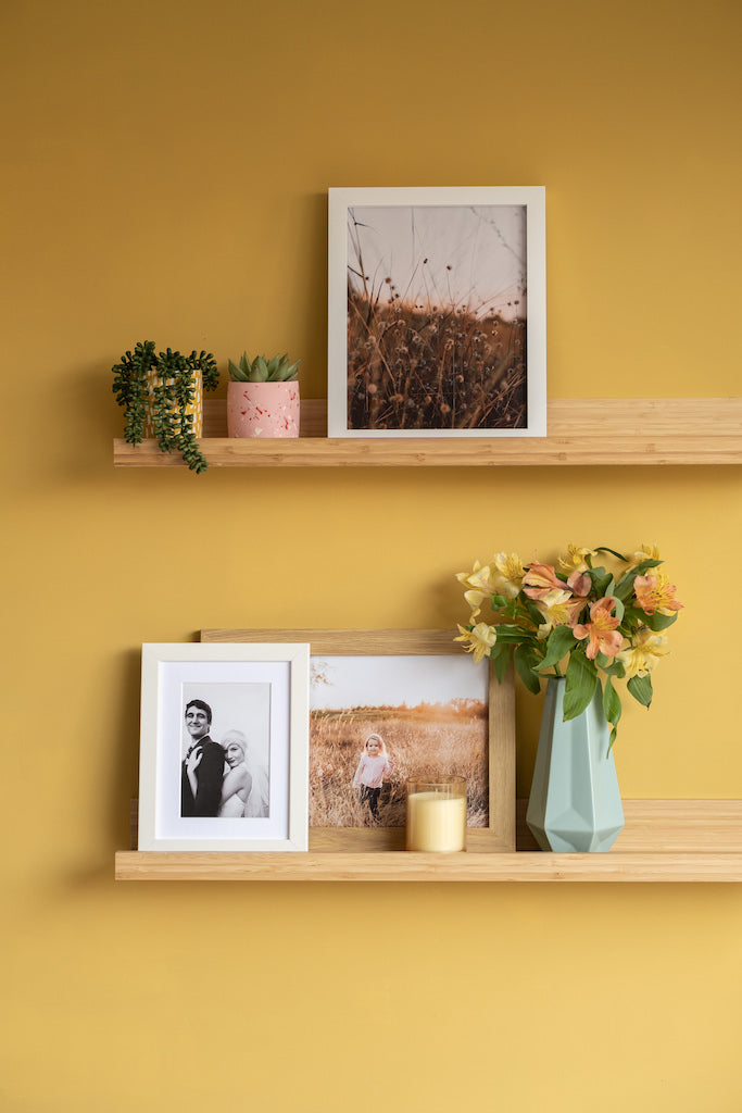 Framed photos on shelf mounted on yellow wall.