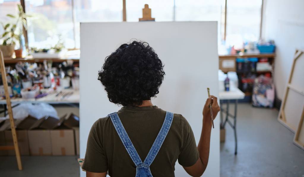 Artist holding brush standing in front of blank canvas