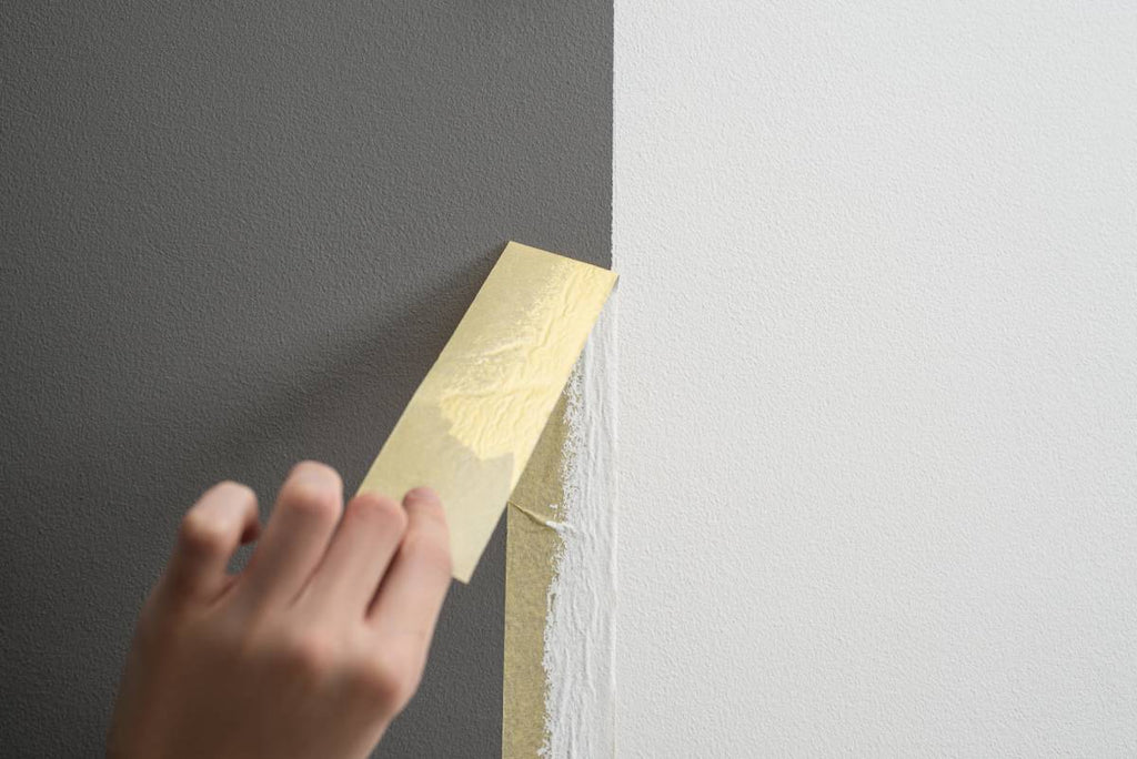Person removing masking tape to show clean line between paint colors