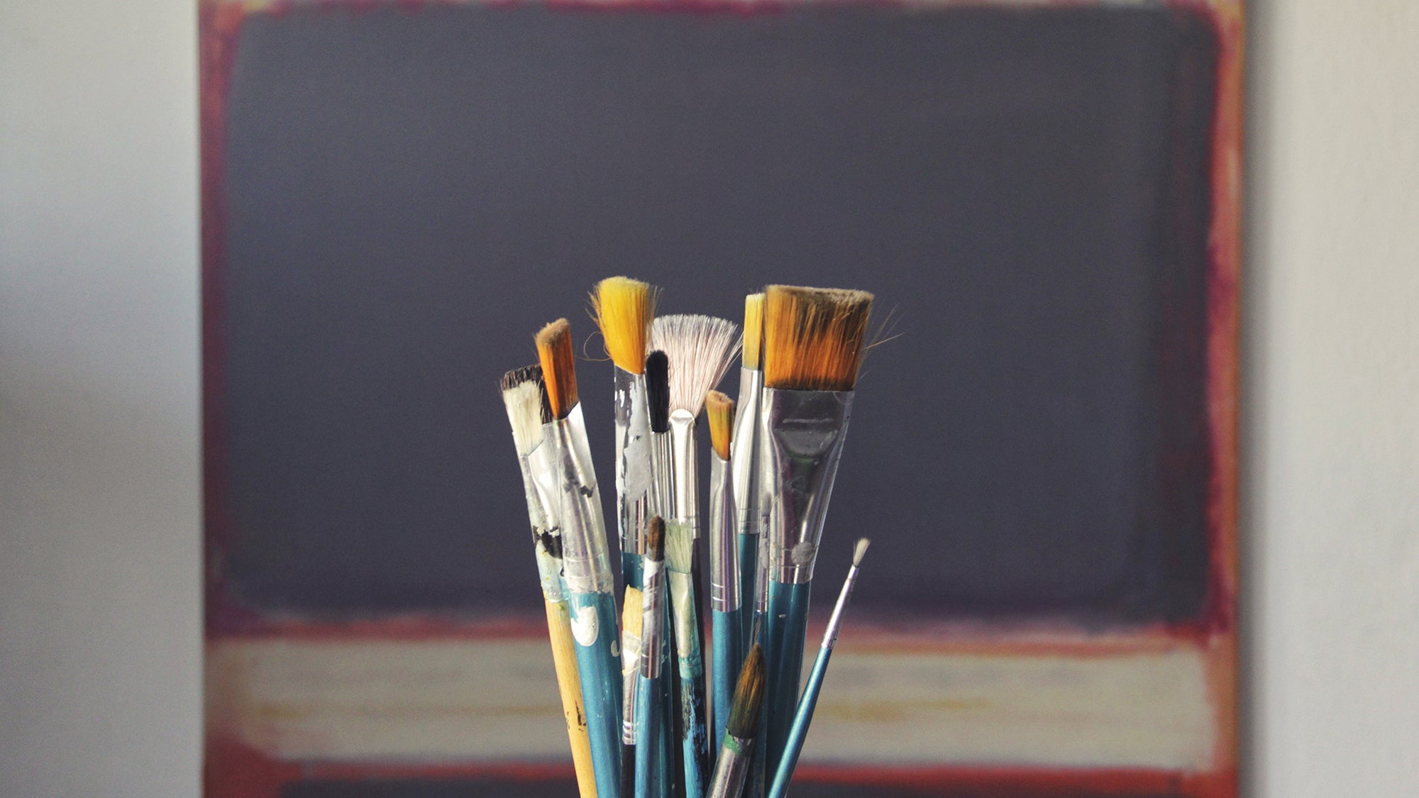 paint brushes displayed in front a piece of painted artwork